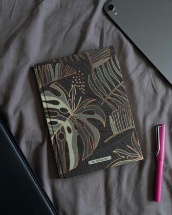 Ein Notizbuch aus Graspapier von Matabooks mit Dschungel-Design. Daneben liegt ein Füller und ein iPad.